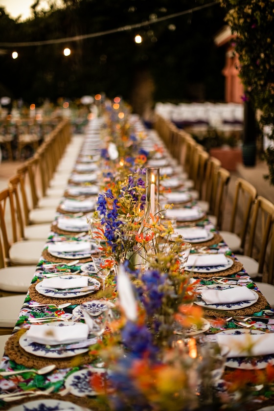 Prospettiva serale della lunga tavolata illuminata da candele e luci sospese. - ACCAELLE Events | Organizzazione eventi e Wedding planner