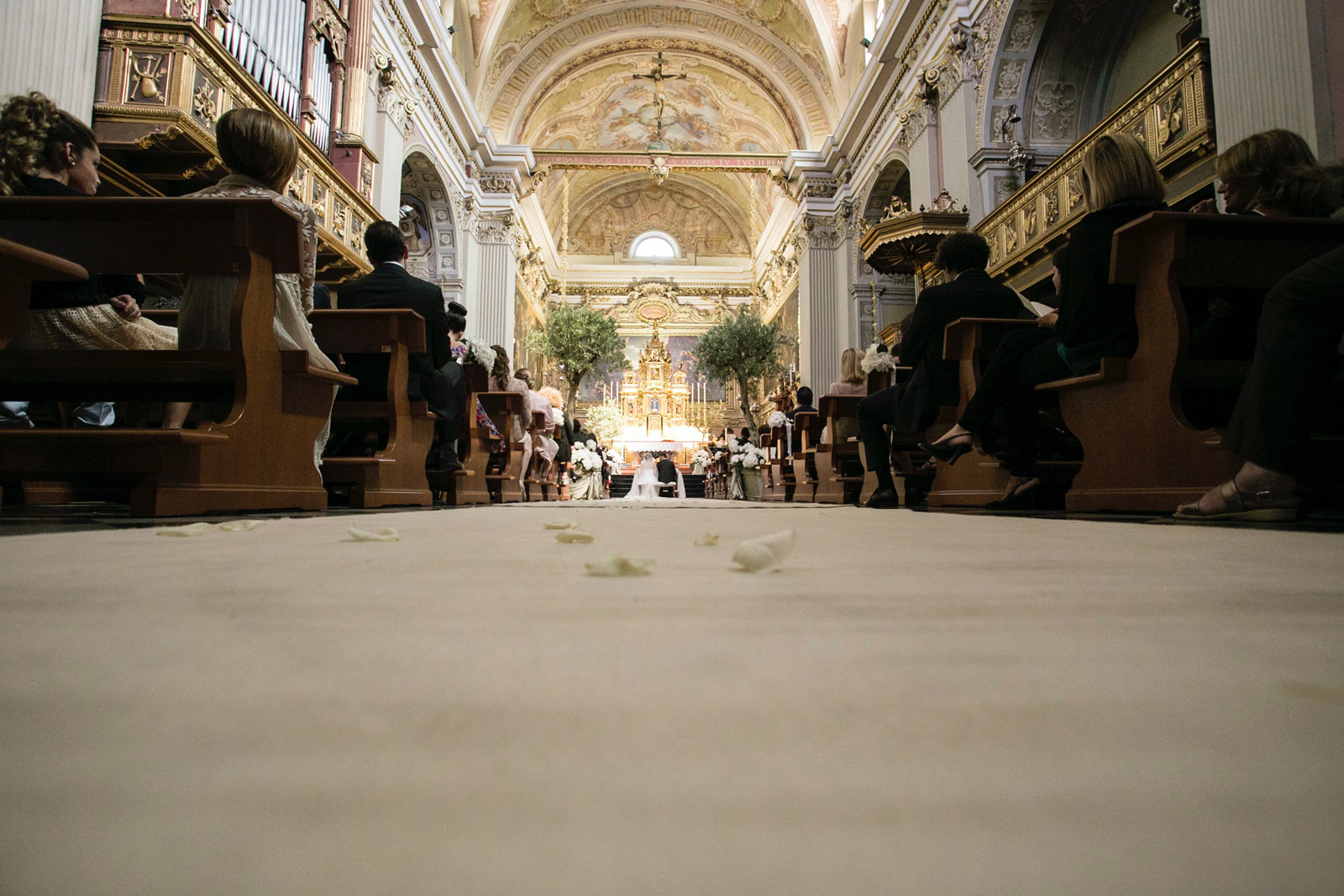 Ripresa dal basso navata centrale, fiori come ornamenti e altare con sposi sullo sfondo - ACCAELLE Events | Organizzazione eventi e Wedding planner