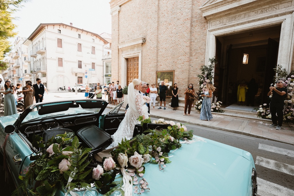 Sposa che scende da un auto azzurra dirigendosi all'entrata di una chiesa  - ACCAELLE Events | Organizzazione eventi e Wedding planner