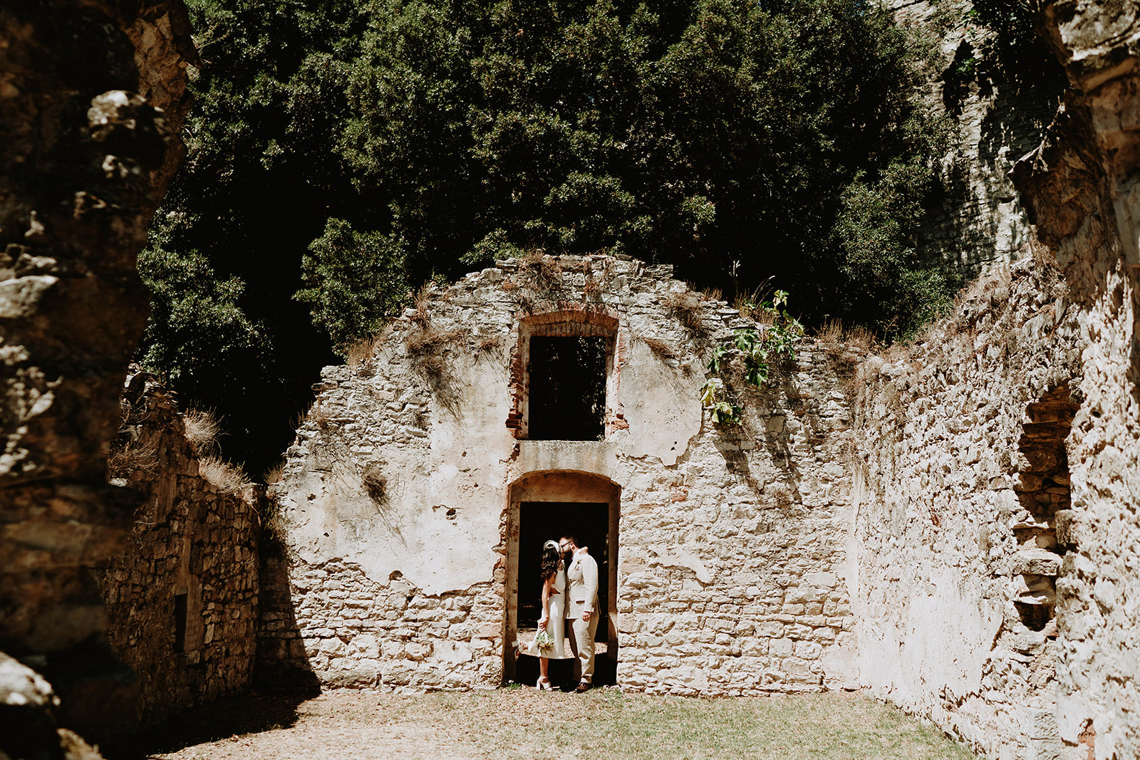 Sposi che si baciano all'entrata di un edificio rustico abbandonato con foresta sullo sfondo durante il giorno - ACCAELLE Events | Organizzazione eventi e Wedding planner