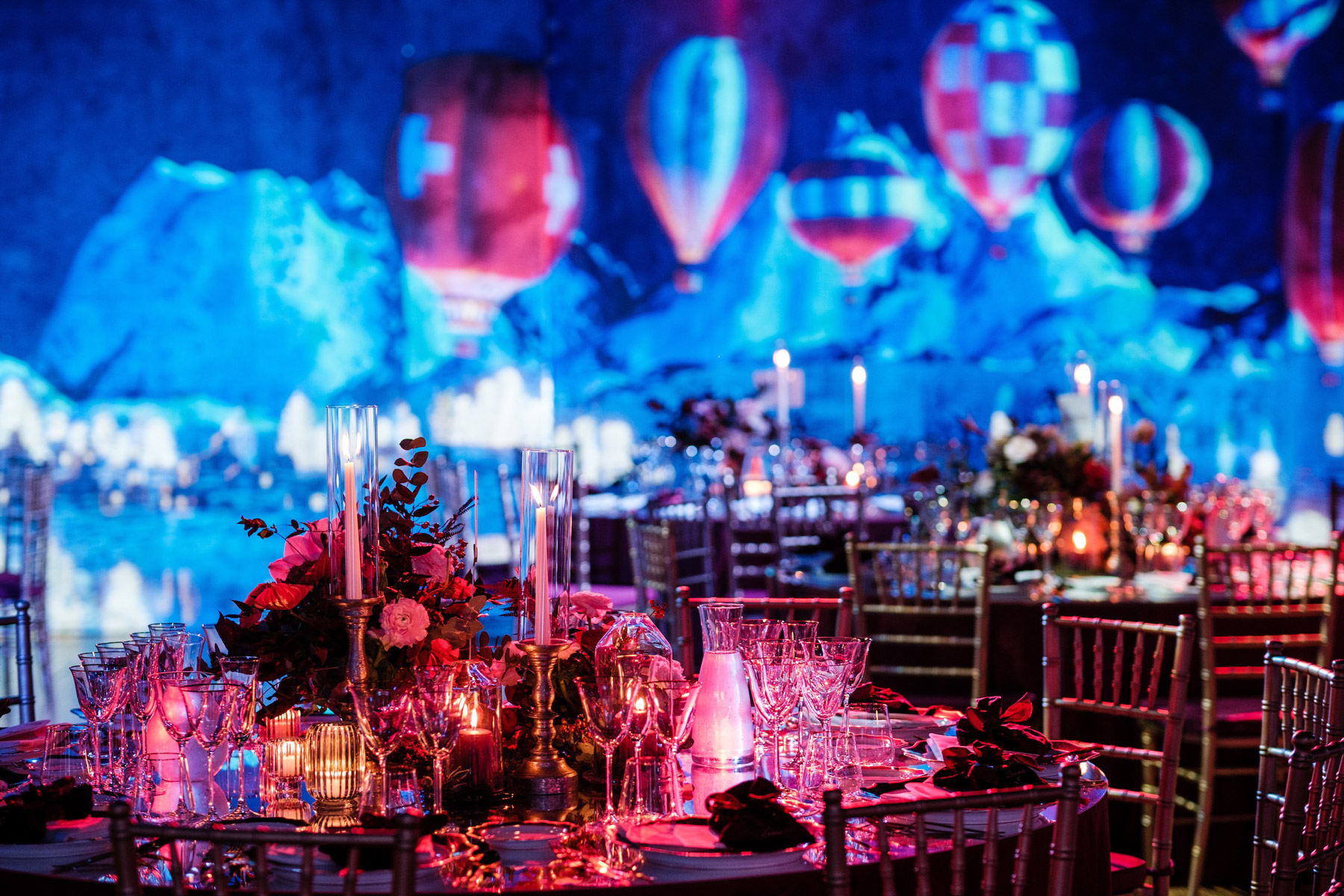 Tavoli da gala ricchi di candele e dettagli floreali immersi in un'illuminazione blu e rossa - ACCAELLE Events | Organizzazione eventi e Wedding planner