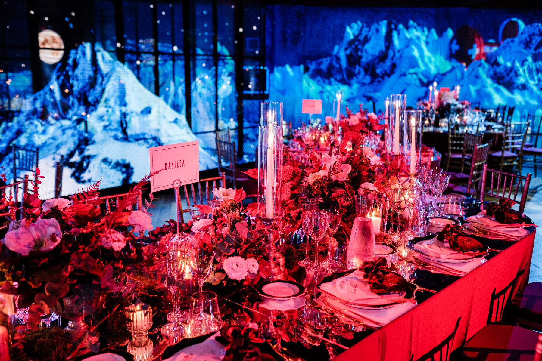 Tavolo allestito con decorazioni floreali illuminato da luci rosse e pareti blu con dettagli di montagne bianch - ACCAELLE Events | Organizzazione eventi e Wedding planner