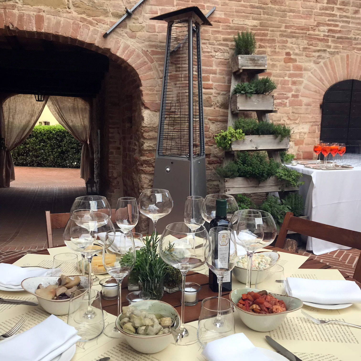 Tavolo imbandito in un cortile rustico vicino a un antico passaggio ad arco in pietra. - ACCAELLE Events | Organizzazione eventi e Wedding planner