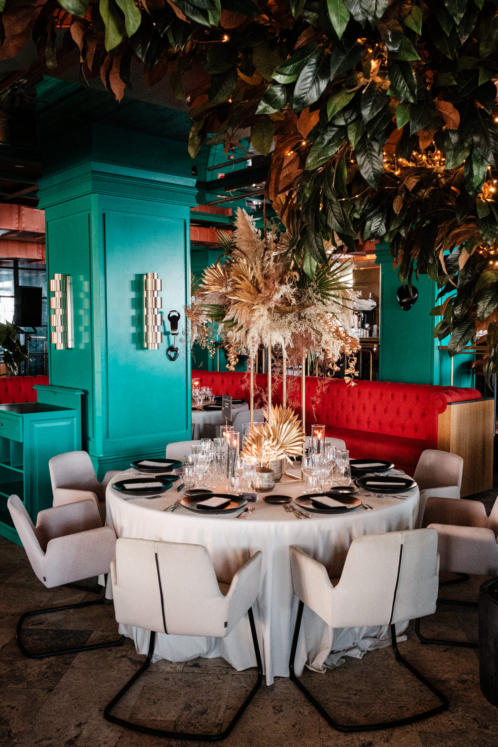 Tavolo rotondo con poltroncine bianche in una sala con pareti color verde acqua, divanetti rossi e composizioni floreali - ACCAELLE Events | Organizzazione eventi e Wedding planner